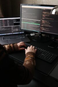 une personne assise à un bureau avec un ordinateur portable et un écran d'ordinateur