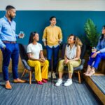 Un groupe diversifié de cinq professionnels participant à une réunion informelle en intérieur, souriant et discutant.
