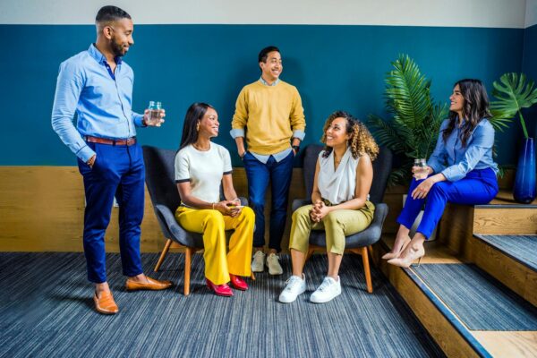 Un groupe diversifié de cinq professionnels participant à une réunion informelle en intérieur, souriant et discutant.
