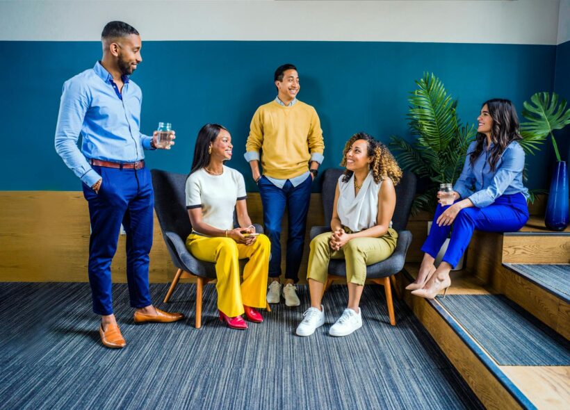 Un groupe diversifié de cinq professionnels participant à une réunion informelle en intérieur, souriant et discutant.