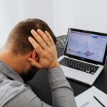 Un homme stressé assis à son bureau regarde les graphiques boursiers en baisse sur son ordinateur portable, indiquant une perte financière.