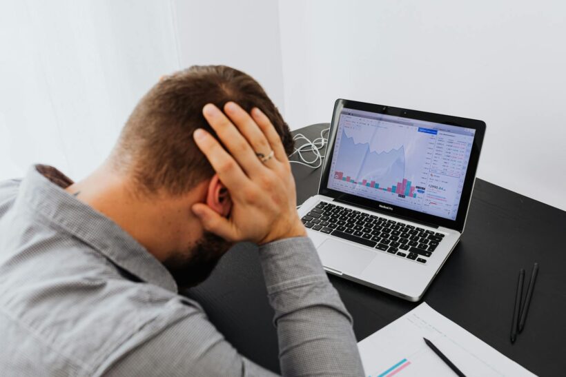 Un homme stressé assis à son bureau regarde les graphiques boursiers en baisse sur son ordinateur portable, indiquant une perte financière.
