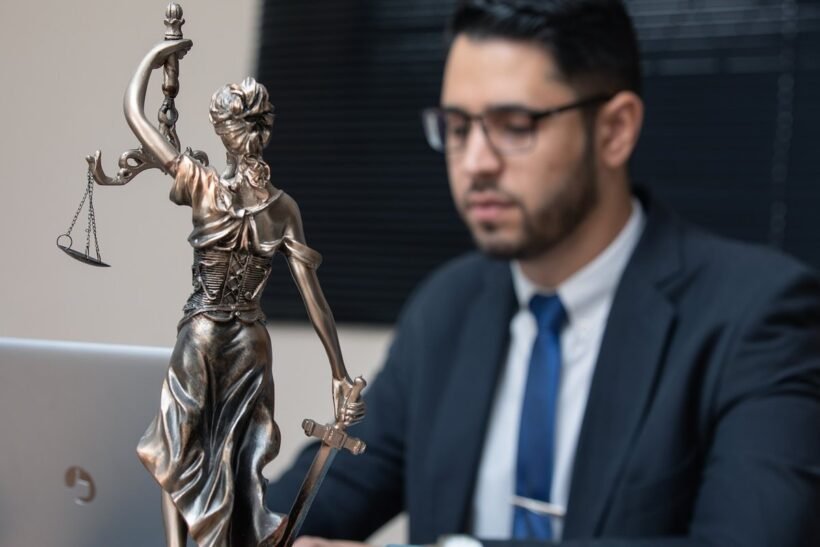 Homme en costume bleu assis près d'une statue de la Justice tenant une balance et une épée
