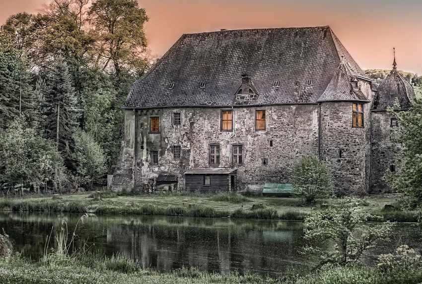Maison en pierre avec toit d'ardoise au bord d'un étang, entourée d'arbres Maison en pierre avec toit d'ardoise au bord d'un étang, entourée d'arbres