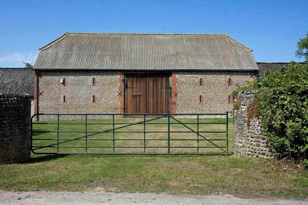 Grange en pierre avec toit métallique, porte en bois, portail fermé, pelouse verte