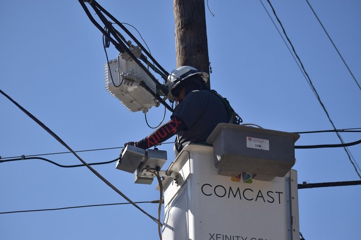 Technicien Comcast sur une électricité, inspectant des câbles sous un ciel bleu
