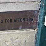 Plaque métallique sur mur en béton à côté d'une porte verte avec bouton